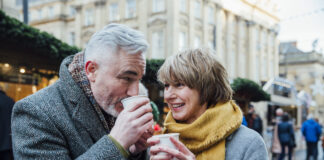 Mature couple are drinking hot drinks in a town christmas market dating