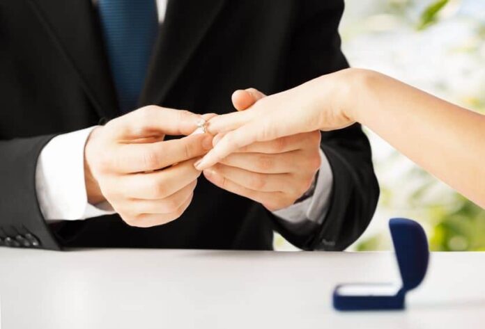 man in black suit proposing to a woman giving her an engagement ring