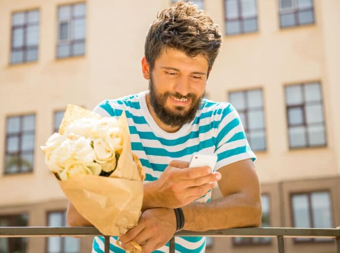 bearded guy holding flowers while texting and hoping to get ex back