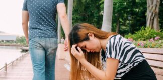 boyfriend breaking up with his girlfriend who is sitting on a bench