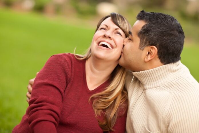 a very happy woman kissed by his husband at the park