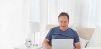 older man wearing blue shirt with laptop in bed