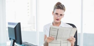 Serious businesswoman wearing glasses holding a newspaper in bright office