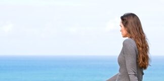 A beautiful sad and unhappy young woman sitting in the green grass looking at the ocean