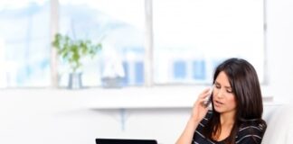 woman stting on a couch talking with someone while using her laptop