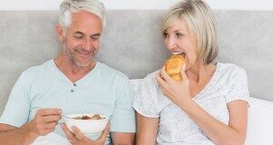 Happy mature couple having breakfast in bed at home