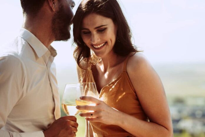 A couple enjoying a romantic getaway smiles with wine glasses in their hands