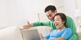 young couple sitting on the couch watching on their laptop, laughing