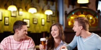 woman in between two men, having dinner while drinking beer