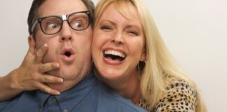 a grinning blonde woman embracing closely a man with an eyeglasses