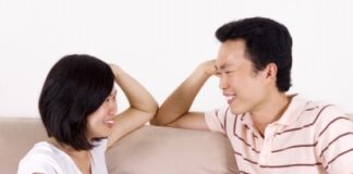 young Asian couple sitting on the sofa, smiling at each other