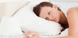 Red-haired woman lying in bed turning off alarm clock