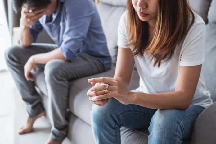 A couple sits on a couch going over the signs of an unhappy marriage