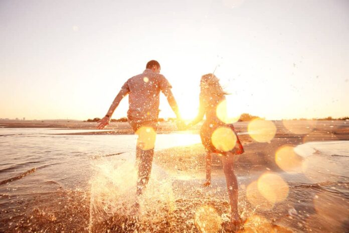 A happy couple runs on a beach after practicing self care in marriage