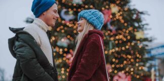 A couple gazes into each others eyes in front of a Christmas tree in one of the most romantic Christmas destinations in the USA