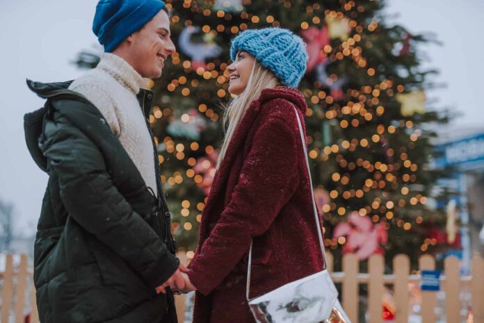 A couple gazes into each others eyes in front of a Christmas tree in one of the most romantic Christmas destinations in the USA