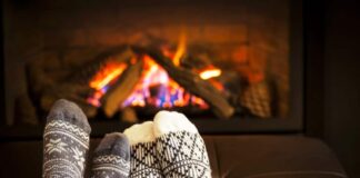Two pairs of feet with socks in front of a fire as a couple watches romantic Christmas movies