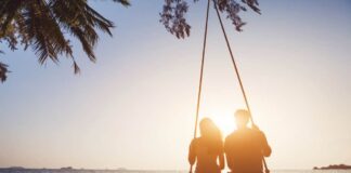A couple swings on a beach at sunset for their couples bucket list