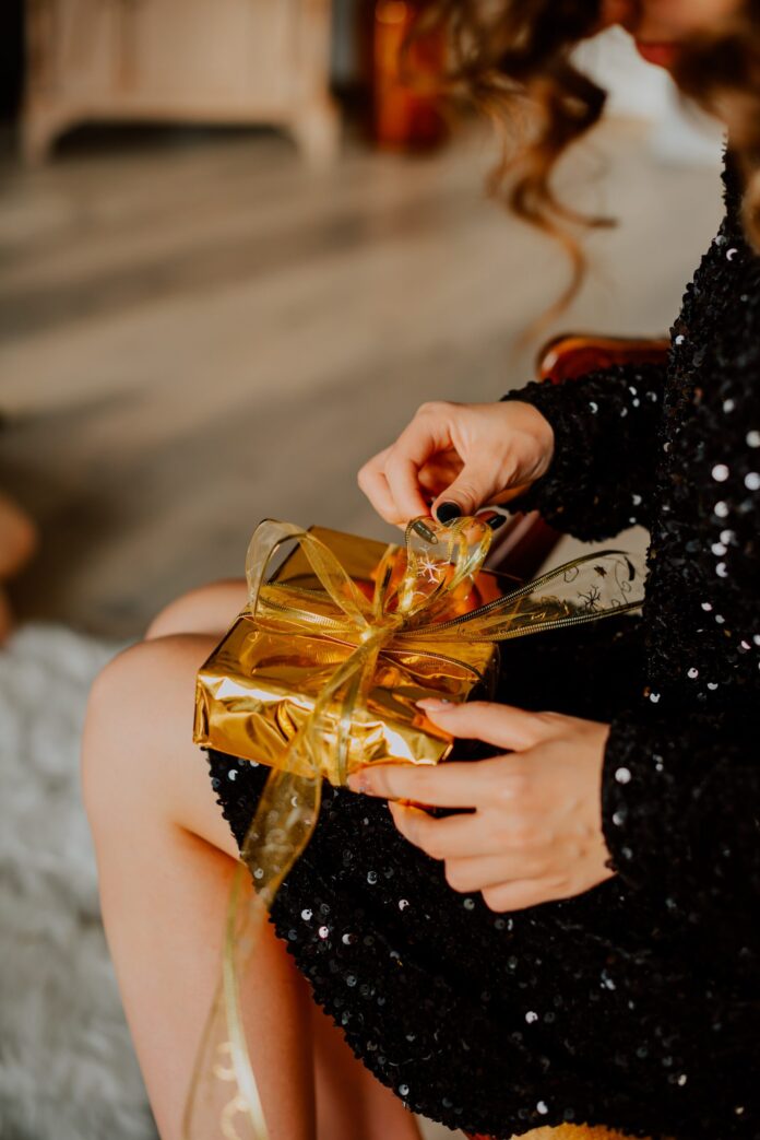 woman in a black dress opening a present wrapped in gold paper on new years