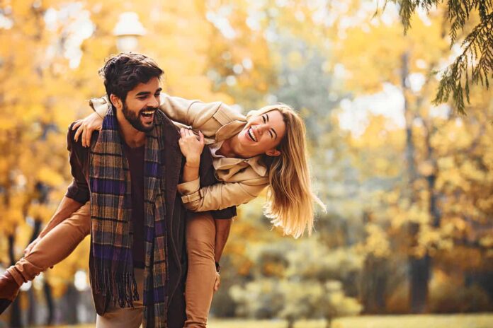 conversation starters for couples image - couple playing in the autumn, blond woman taking piggyback ride from bearded man