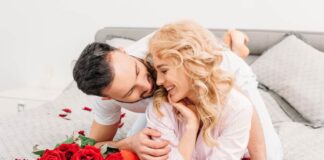 valentine's day date ideas - couple cuddling on bed next to bright red bouquet of roses