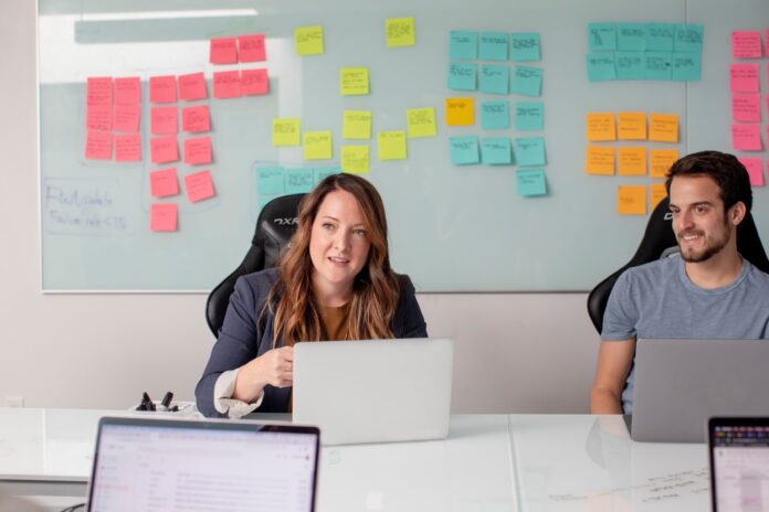 male and female employees with computers sitting in front of a white board covered in post-it notes