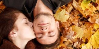 the cutest fall date ideas - couple laying on fall leaves, girl kissing boy's cheek