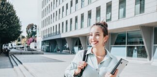 brunette college girl holding textbooks outside of a school building