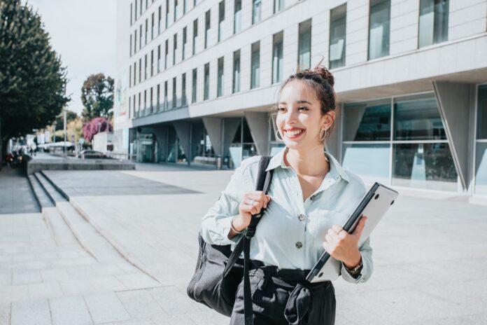 brunette college girl holding textbooks outside of a school building