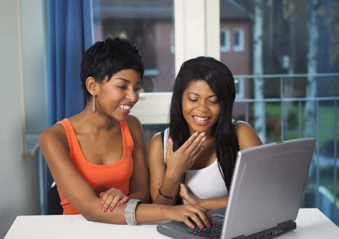 two women smiling while looking at the computer