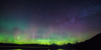 A purple and green sky reflected in a lake in Montana, one of the best places to see the Northern Lights in the USA