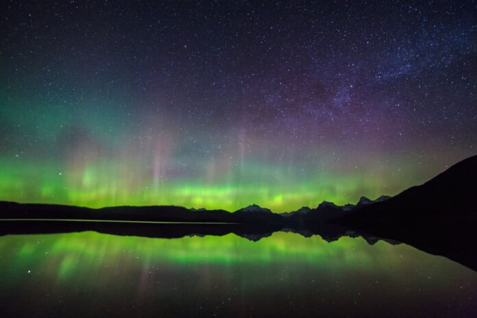 A purple and green sky reflected in a lake in Montana, one of the best places to see the Northern Lights in the USA