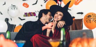 A couple is sitting while dressed in Halloween costumes surrounded by orange balloons.