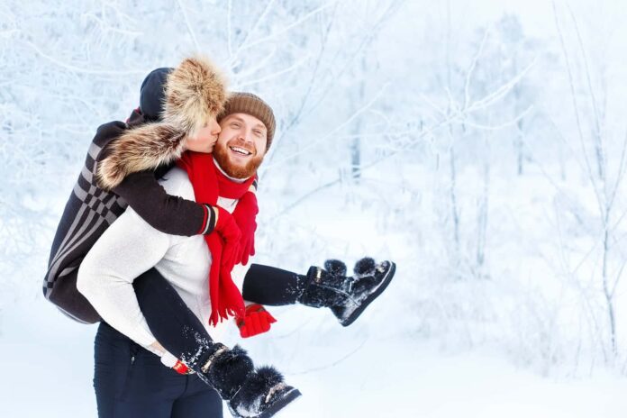 A man gives a woman a piggyback ride on a winter day surrounded by trees.